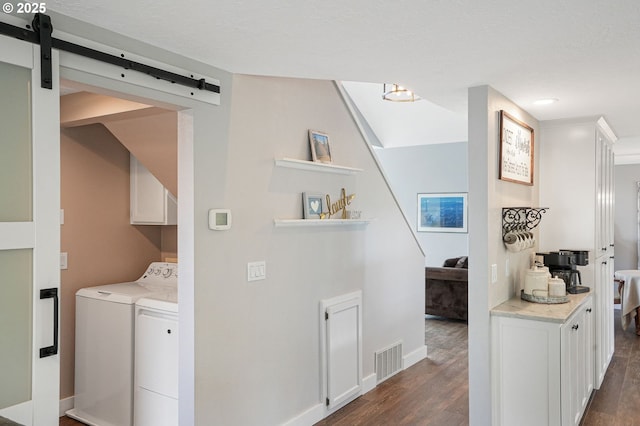 clothes washing area with washer and dryer, visible vents, dark wood finished floors, and a barn door