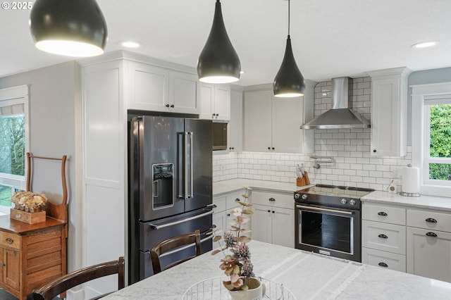 kitchen featuring tasteful backsplash, white cabinetry, high quality fridge, wall chimney range hood, and stainless steel range with electric stovetop