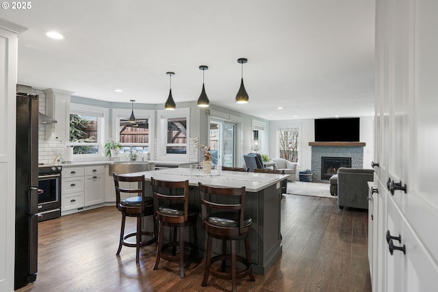 kitchen with dark wood-type flooring, a fireplace, white cabinetry, a center island, and black appliances