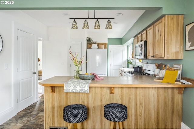 kitchen featuring a peninsula, freestanding refrigerator, gas range, stainless steel microwave, and a kitchen breakfast bar