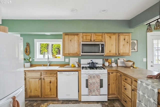 kitchen with light countertops, a peninsula, stone finish floor, white appliances, and a sink