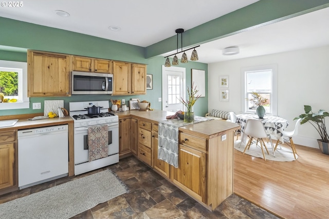 kitchen featuring decorative light fixtures, light countertops, a peninsula, stone finish floor, and white appliances