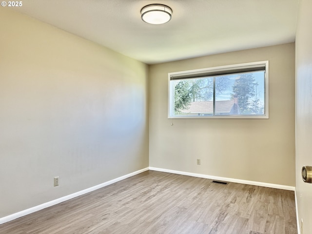 empty room featuring wood finished floors, visible vents, and baseboards