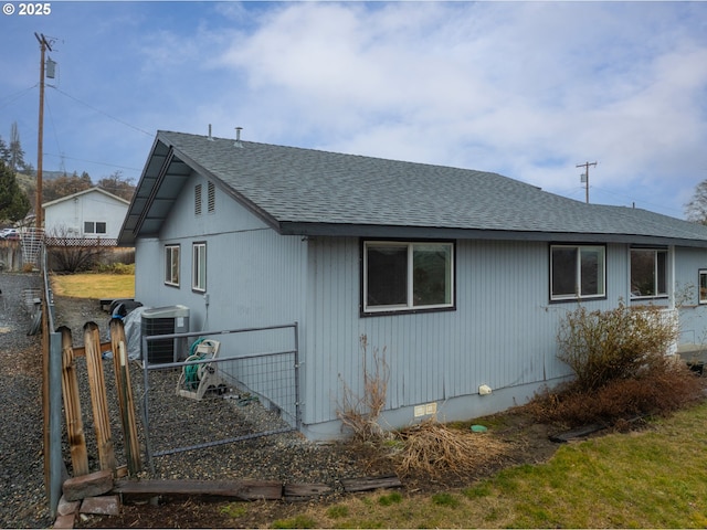 view of side of property with a shingled roof, crawl space, and fence