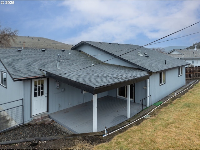 view of side of home featuring entry steps, a shingled roof, a lawn, and fence