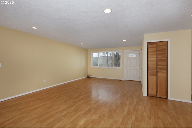 unfurnished living room featuring a textured ceiling, light wood-type flooring, and baseboards