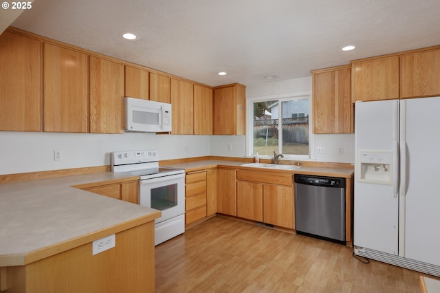 kitchen featuring light wood finished floors, light countertops, white appliances, and a sink