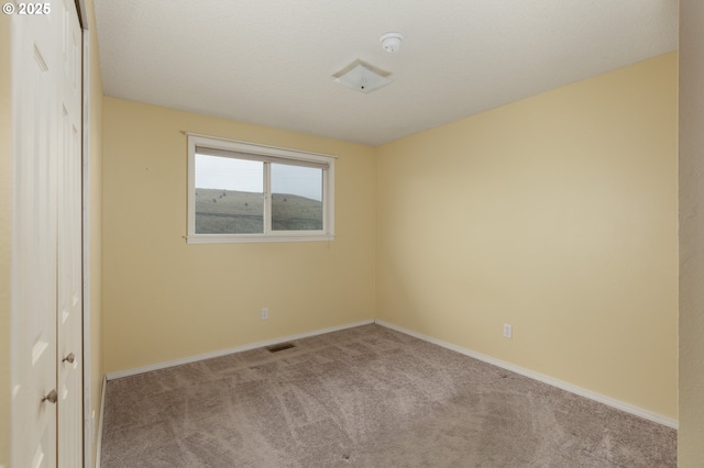 empty room featuring light colored carpet, visible vents, and baseboards