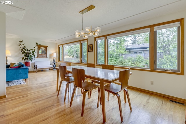 dining space featuring visible vents, an inviting chandelier, baseboards, light wood-type flooring, and a textured ceiling