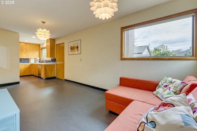 living area with concrete flooring, baseboards, a notable chandelier, and a healthy amount of sunlight