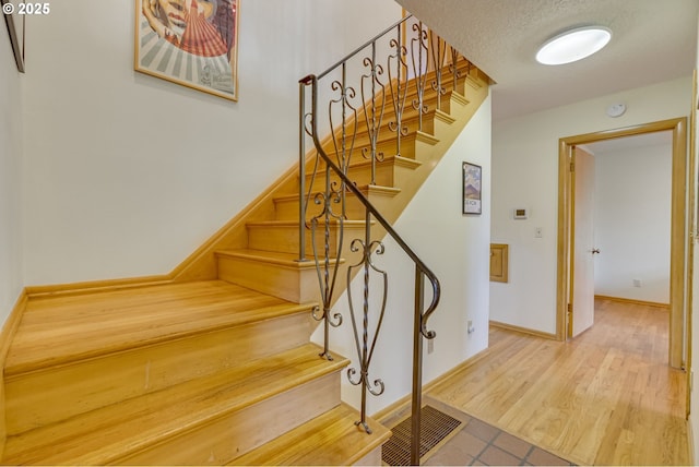 stairway featuring baseboards, a textured ceiling, and wood finished floors