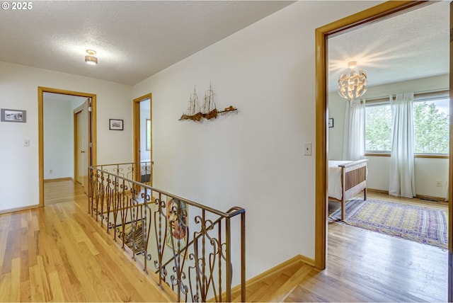 hall with wood finished floors, baseboards, a textured ceiling, and an upstairs landing