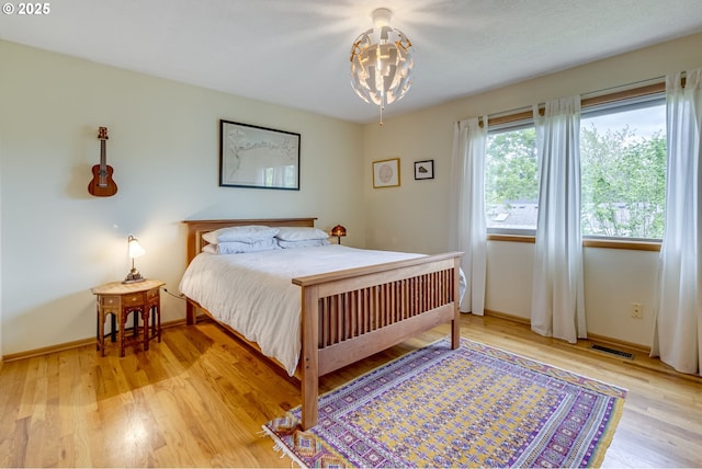 bedroom with baseboards, a notable chandelier, light wood-style flooring, and visible vents