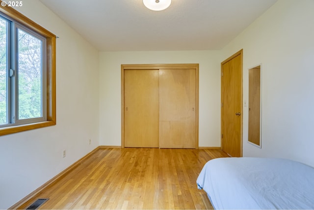 bedroom featuring light wood-style floors, baseboards, visible vents, and a closet