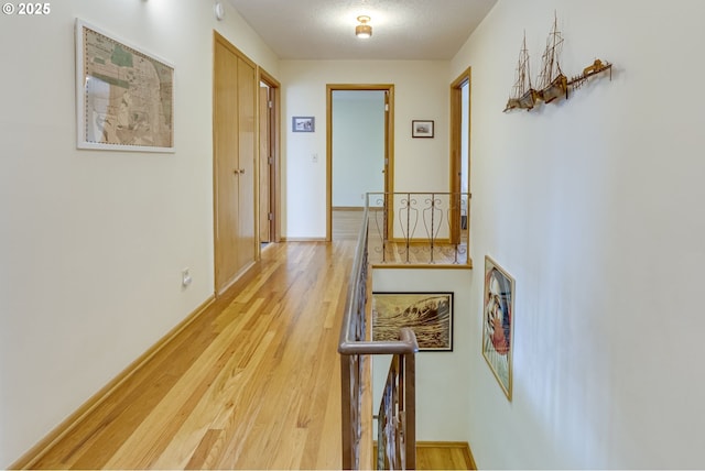 hallway with light wood-type flooring, a textured ceiling, baseboards, and an upstairs landing