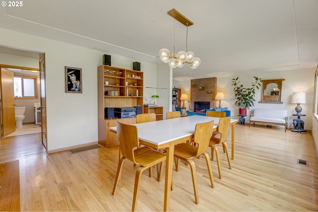 dining room featuring visible vents, a brick fireplace, baseboards, a chandelier, and light wood-style flooring