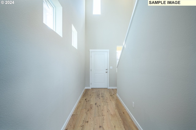 corridor with a high ceiling, light wood-style flooring, and baseboards