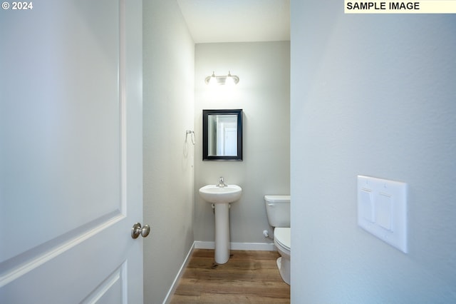 bathroom with toilet, a sink, baseboards, and wood finished floors