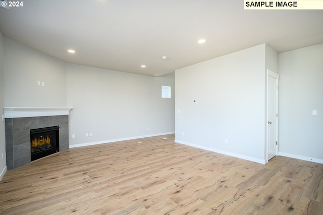 unfurnished living room with light wood-style floors, a tile fireplace, and recessed lighting