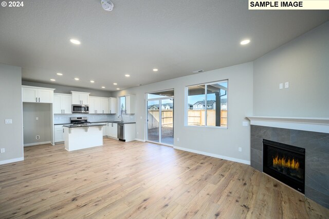 kitchen featuring stainless steel appliances, white cabinets, open floor plan, dark countertops, and a tiled fireplace