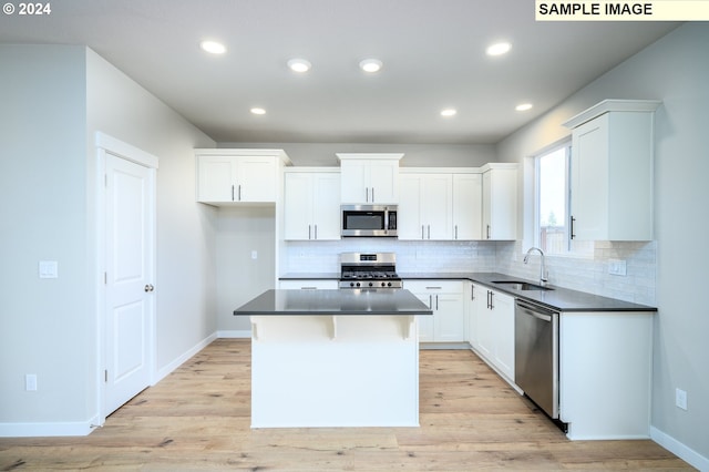 kitchen with white cabinets, dark countertops, a kitchen island, stainless steel appliances, and a sink