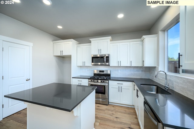 kitchen featuring dark countertops, appliances with stainless steel finishes, light wood-style floors, white cabinetry, and a sink