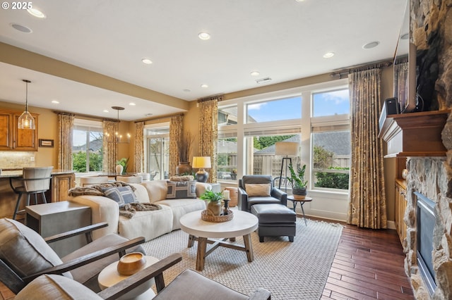 living area featuring a stone fireplace, baseboards, recessed lighting, dark wood-type flooring, and visible vents