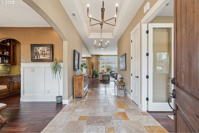 entrance foyer featuring an inviting chandelier, ornamental molding, visible vents, arched walkways, and stone tile floors