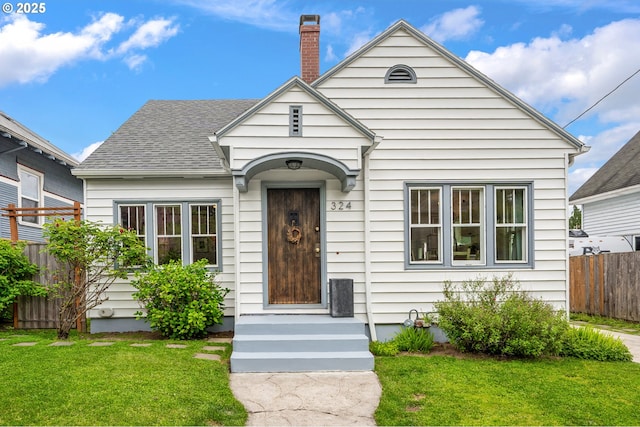 bungalow-style home featuring a chimney, roof with shingles, fence, and a front yard
