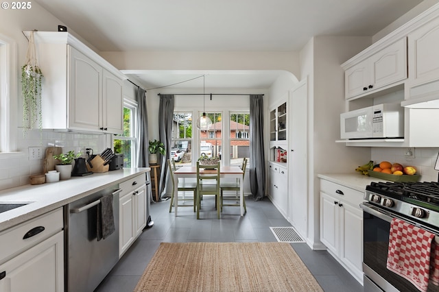 kitchen with appliances with stainless steel finishes, light countertops, tile patterned floors, white cabinetry, and backsplash