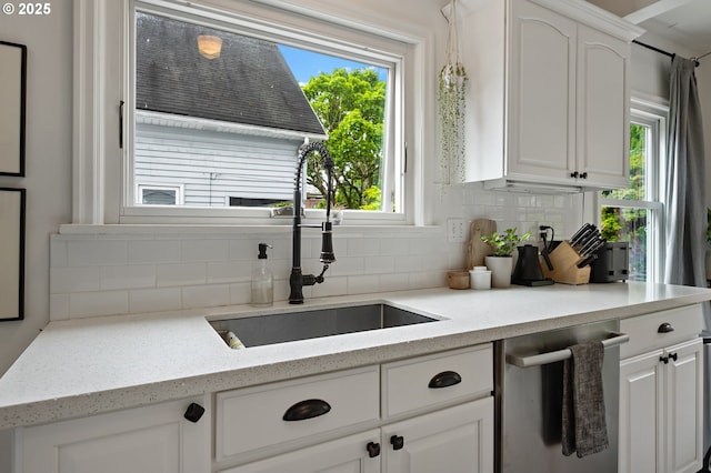 kitchen with white cabinets, tasteful backsplash, light stone counters, a sink, and dishwasher