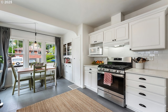 kitchen featuring stainless steel gas range, light countertops, decorative backsplash, white microwave, and under cabinet range hood