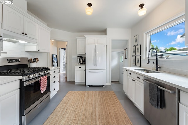 kitchen with white cabinets, appliances with stainless steel finishes, a sink, backsplash, and under cabinet range hood