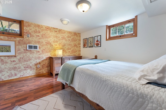 bedroom with baseboards, wallpapered walls, wood finished floors, and visible vents