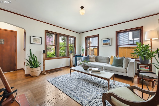 living room featuring crown molding, visible vents, wood finished floors, baseboards, and arched walkways