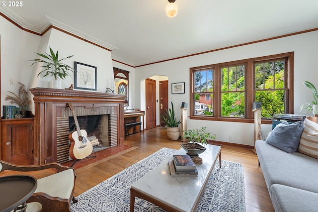 living area with ornamental molding, a brick fireplace, wood finished floors, baseboards, and arched walkways
