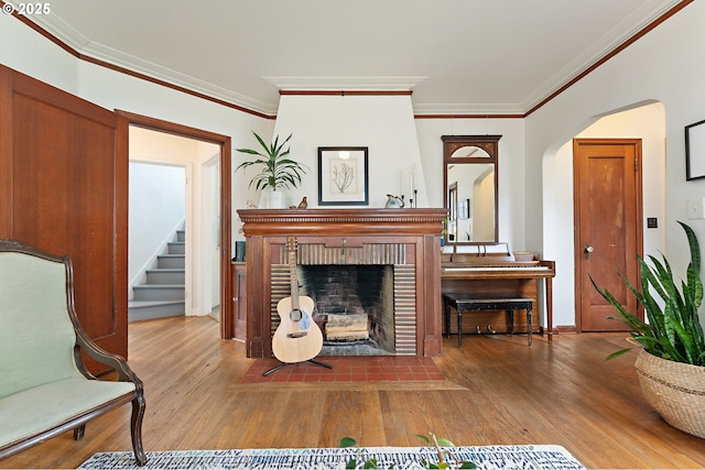 living area with a brick fireplace, arched walkways, crown molding, and wood finished floors
