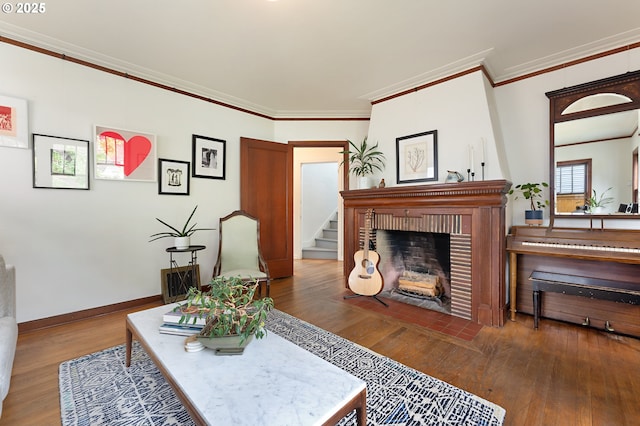 living room featuring crown molding, a brick fireplace, stairs, baseboards, and wood finished floors