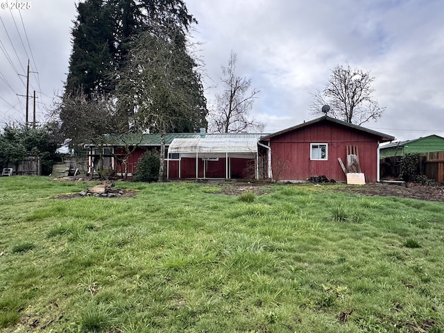 rear view of property featuring an outbuilding, a lawn, and fence