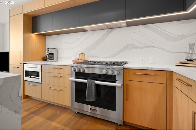 kitchen with modern cabinets, light brown cabinets, high end stainless steel range oven, backsplash, and light wood finished floors