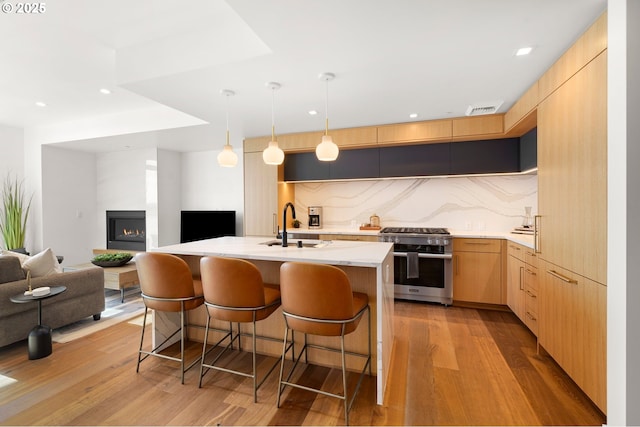 kitchen with light brown cabinetry, a kitchen bar, stainless steel stove, modern cabinets, and a sink