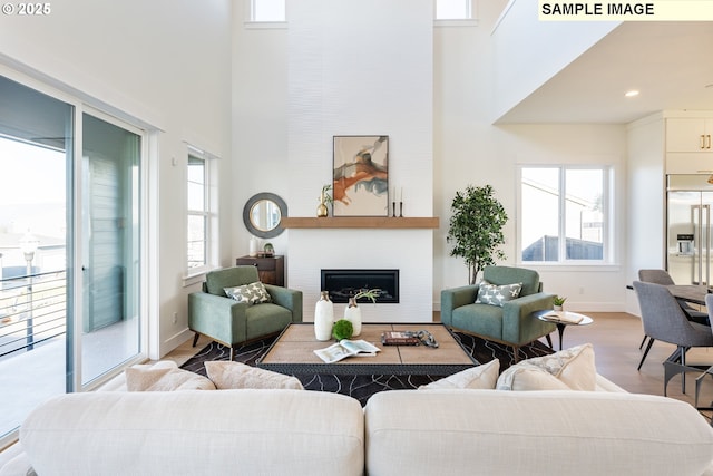 living room with a towering ceiling, wood finished floors, a glass covered fireplace, and baseboards
