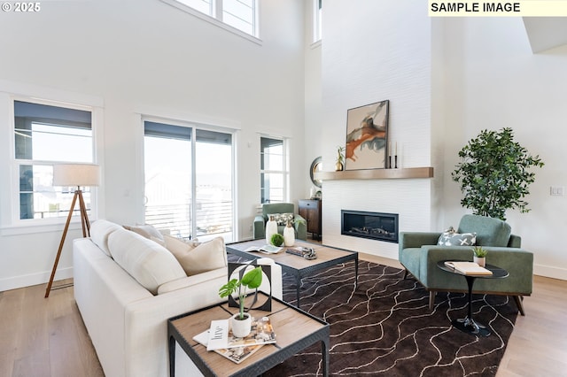 living room featuring healthy amount of natural light, a large fireplace, recessed lighting, wood finished floors, and a high ceiling