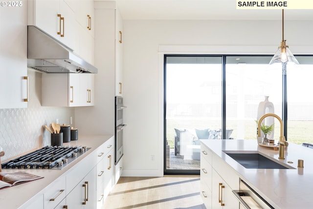 kitchen featuring stainless steel appliances, under cabinet range hood, a sink, light wood-style floors, and a breakfast bar