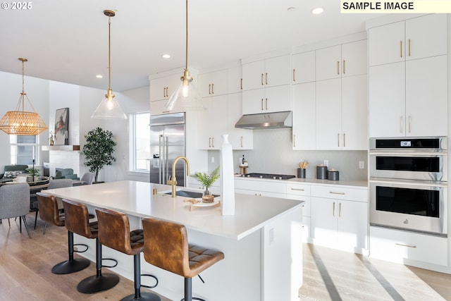 kitchen featuring stainless steel built in refrigerator, a sink, light wood finished floors, tasteful backsplash, and light countertops