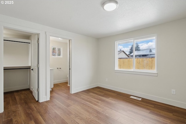 unfurnished bedroom featuring a textured ceiling, a closet, a walk in closet, and wood-type flooring