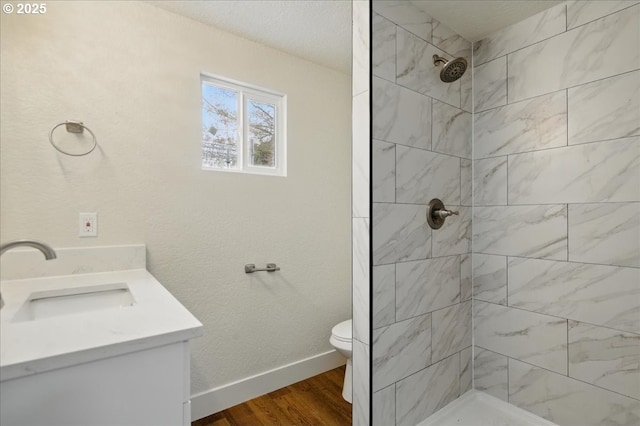 bathroom with hardwood / wood-style flooring, vanity, a tile shower, and toilet