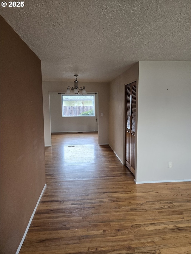 spare room featuring baseboards, a chandelier, a textured ceiling, and wood finished floors