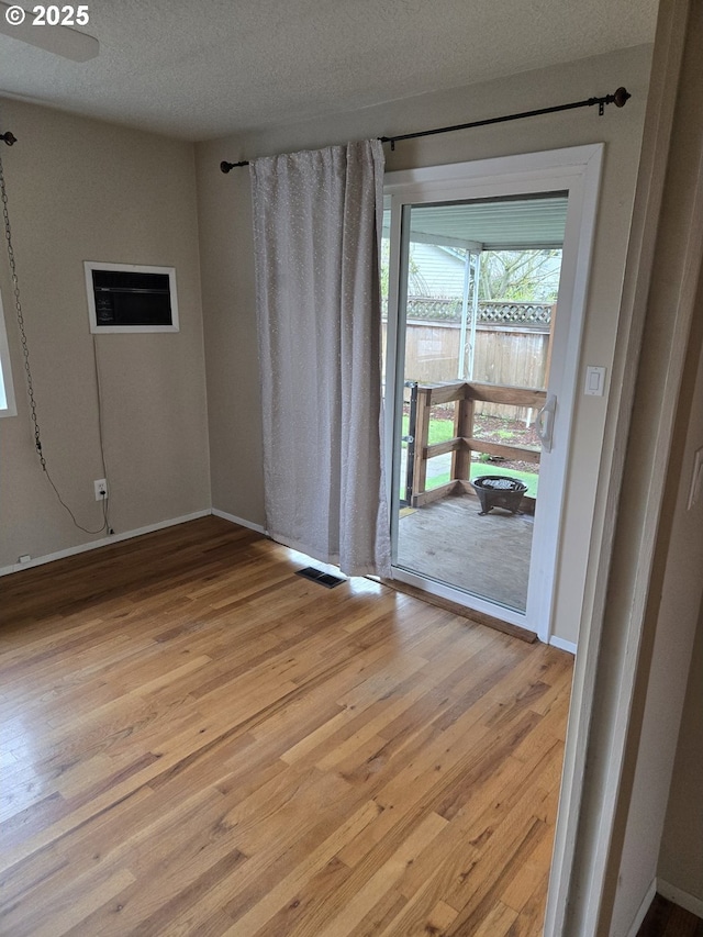 spare room with a textured ceiling, visible vents, light wood-style floors, and baseboards