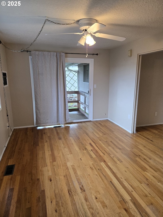 empty room with visible vents, a ceiling fan, a textured ceiling, and wood finished floors